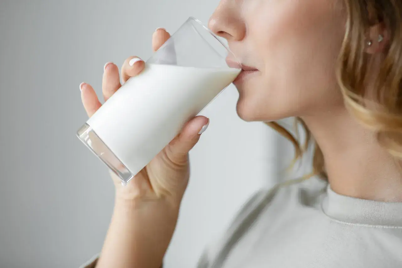 Donna bionda beve un bicchiere di latte. C'è chi dice che il latte fa ingrassare, ma lei sembra goderselo.