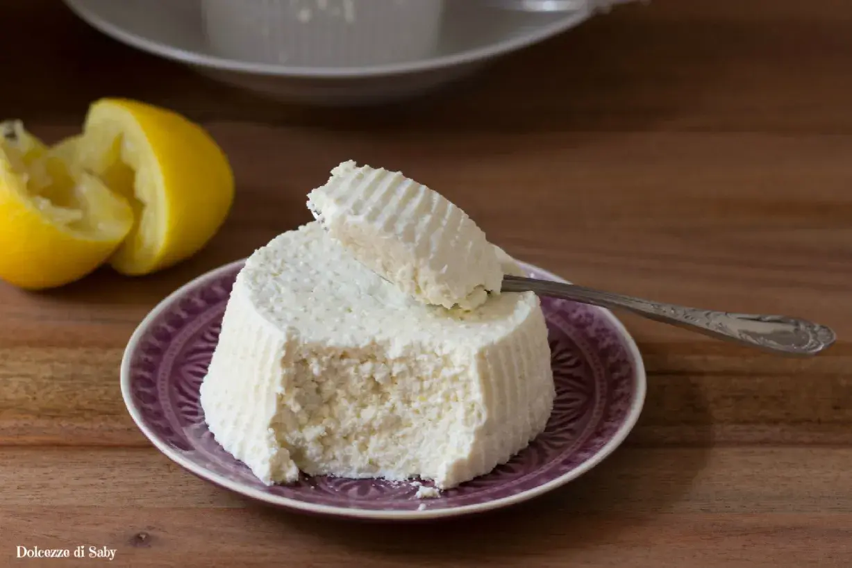 Ricotta fresca su piatto viola, con limone e cucchiaino. Perfetta per ogni ricetta.