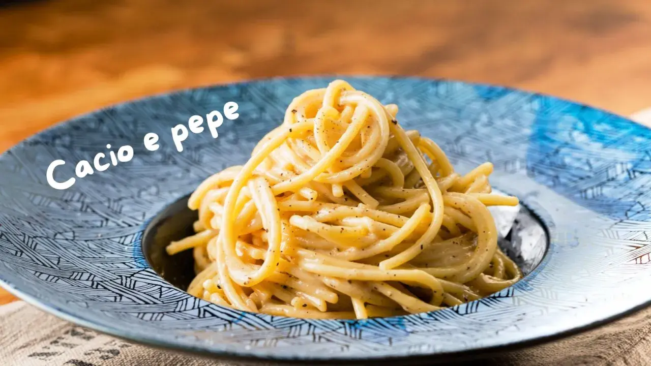 Un piatto di spaghetti fumanti, conditi con una cremosa salsa cacio e pepe, serviti in un piatto blu decorato.
