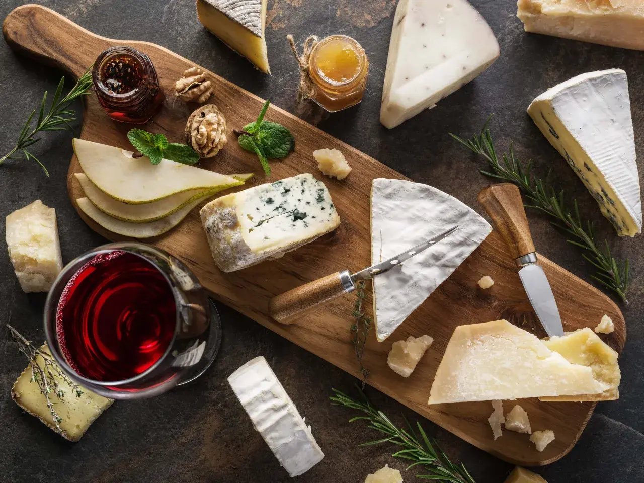 Tagliere con vari formaggi, tra cui un formaggio inglese, pere, noci, miele e vino rosso.