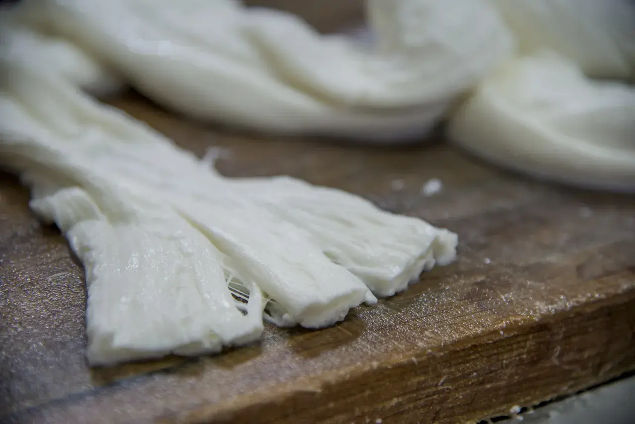 Formaggio a pasta filata, lavorato a mano, con fili bianchi e morbidi su un tagliere di legno.