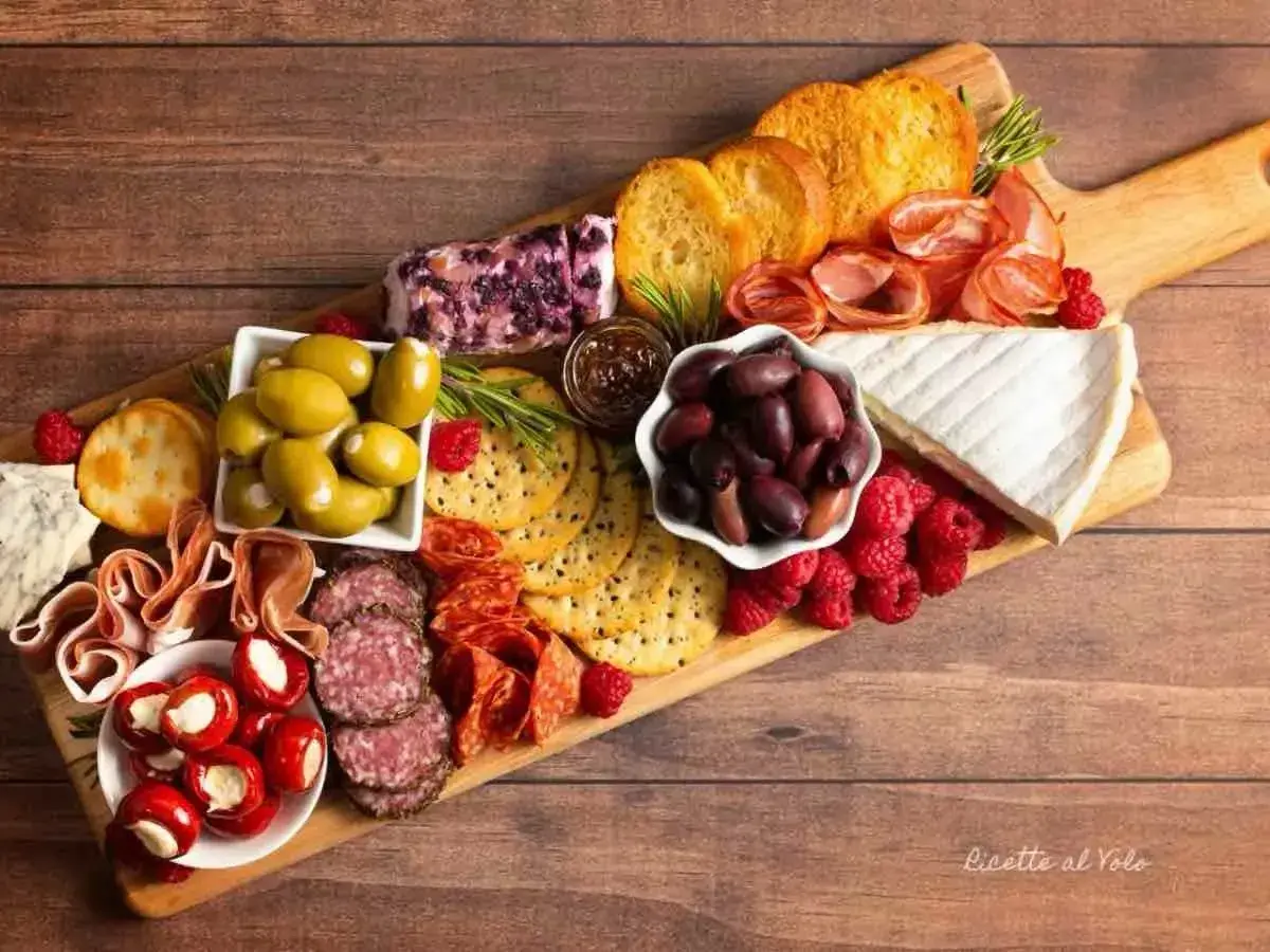 Tagliere ricco di antipasti sfiziosi: salumi, formaggi, olive, lamponi e crostini. Un tripudio di sapori e colori.