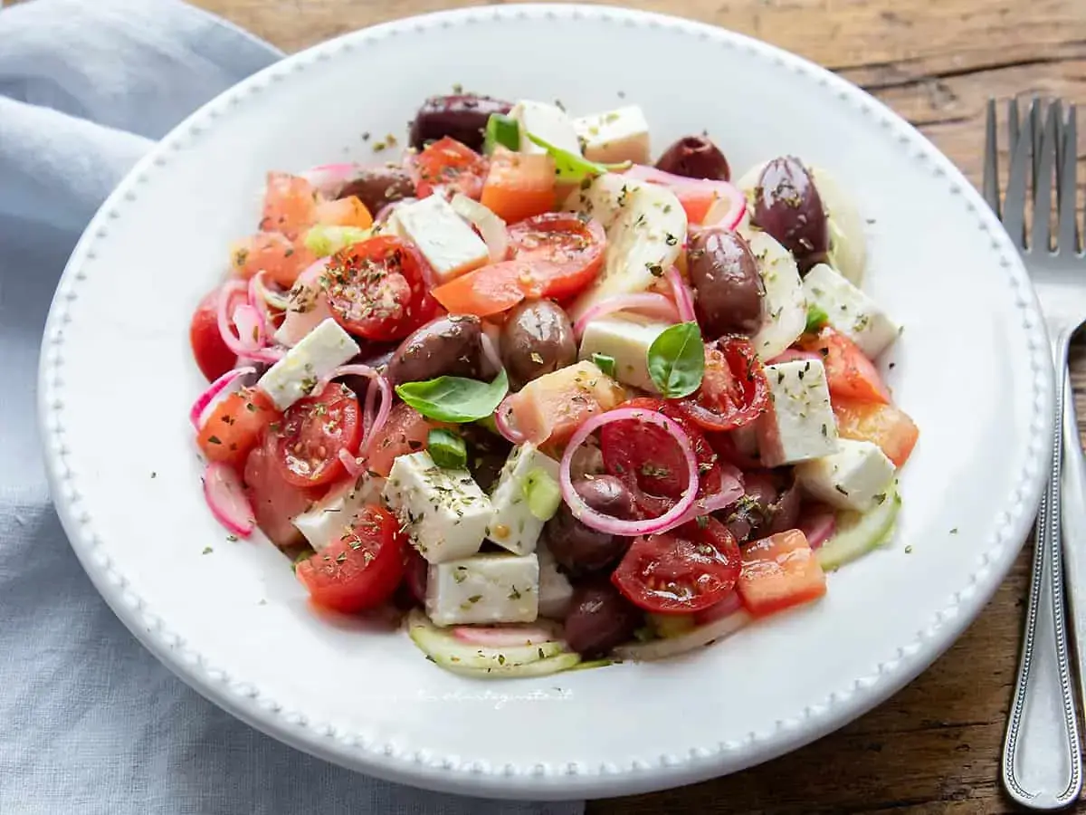 Insalata fresca con pomodorini, olive, cipolla rossa e cubetti di feta, condita con erbe aromatiche.