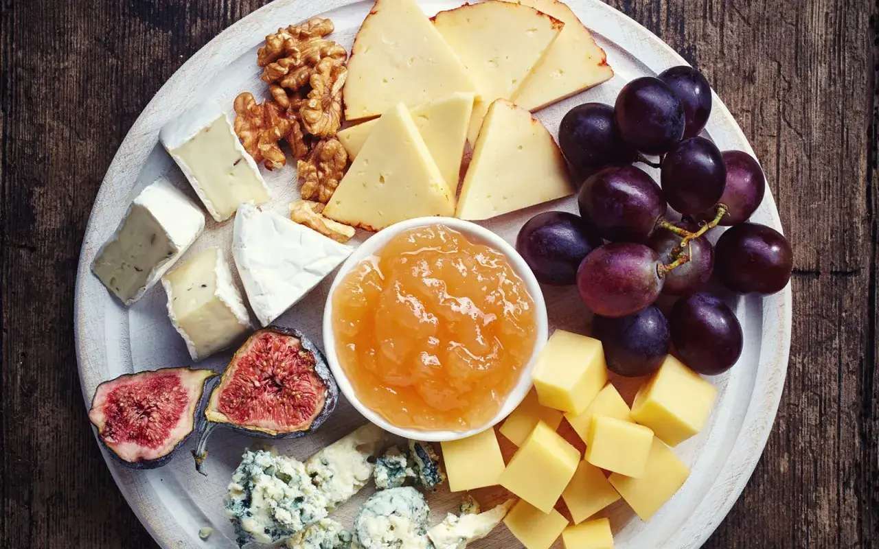 Vassoio con formaggi misti, uva, fichi, noci e una ciotola di composta di pere per formaggi.