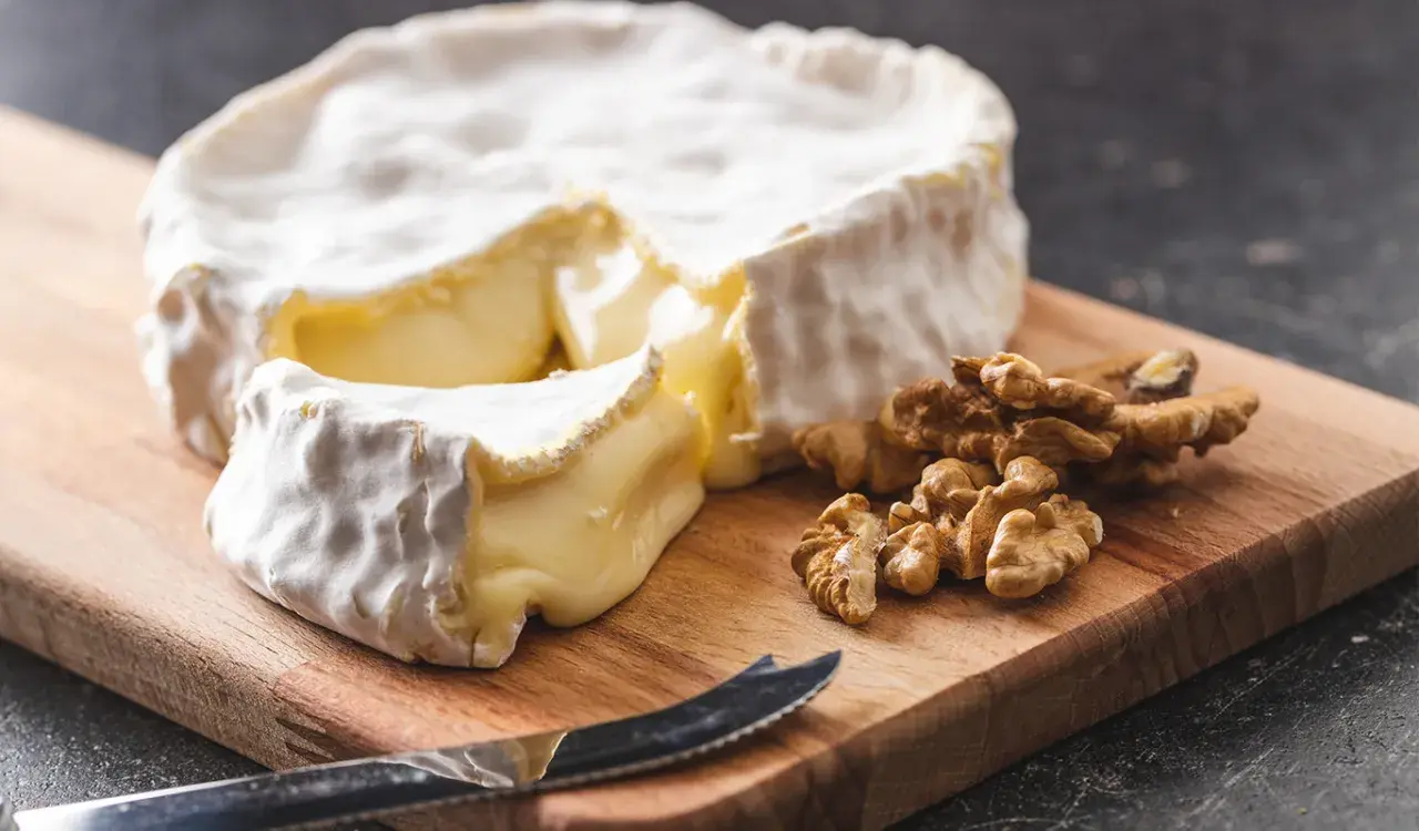 Un pezzo di brie, un formaggio grasso, su un tagliere con noci e un coltello.