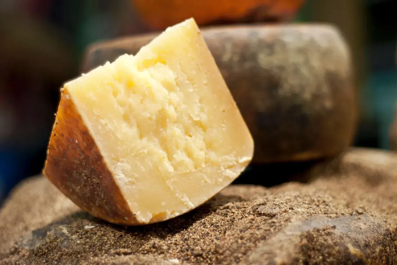Un pezzo di formaggio sardo stagionato, con crosta scura e pasta gialla, riposa su un letto di spezie macinate.