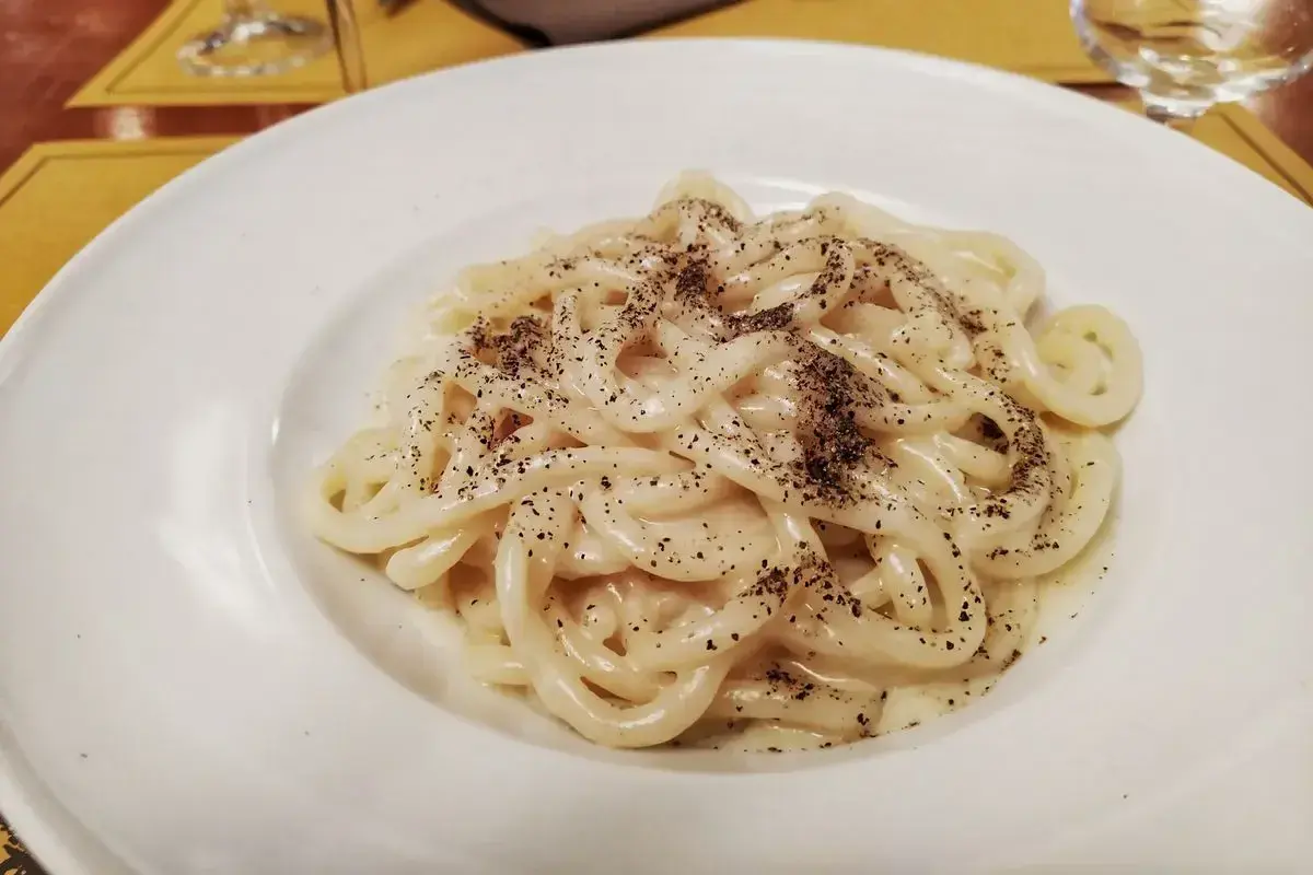 Pici cacio e pepe cremosi e fumanti, un classico della cucina romana, serviti su un piatto bianco.