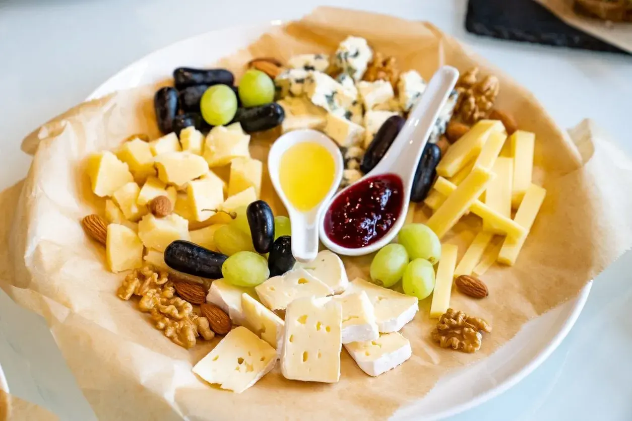 Un tagliere ricco di formaggio semistagionato, uva, noci, mandorle, miele e marmellata.