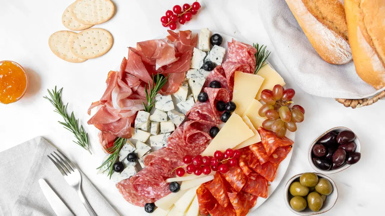 Un invitante piatto di formaggi con salumi, uva, olive e pane croccante, perfetto per un aperitivo.