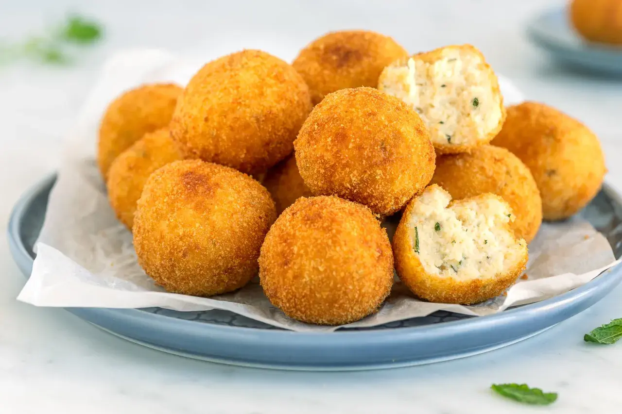 Arancini dorati e croccanti, perfetti per gustose ricette con ricotta. Uno è morso, rivelando un ripieno morbido e saporito.