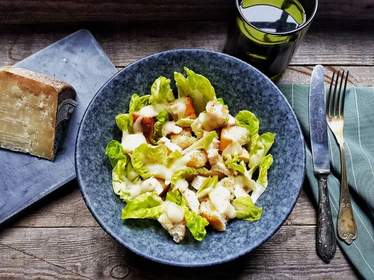 Insalata Caesar con crostini e una generosa spolverata di crema di pecorino. Accanto, un pezzo di formaggio stagionato.