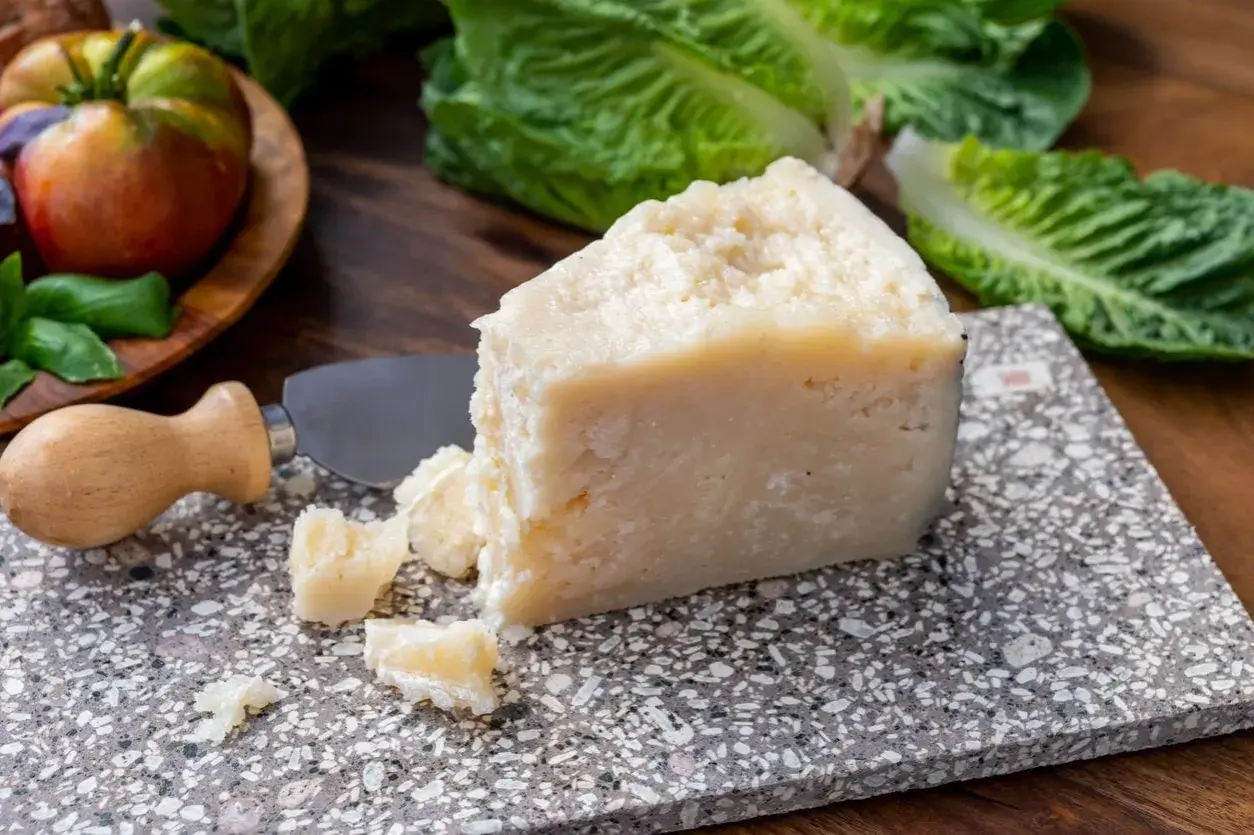 Un pezzo di pecorino siciliano stagionato, pronto per essere gustato con pomodori e lattuga fresca.