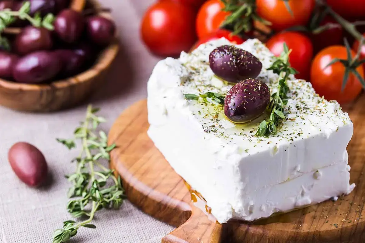 Blocco di feta condito con olive e erbe aromatiche, perfetto per scoprire quante calorie ha la feta in una gustosa insalata greca.