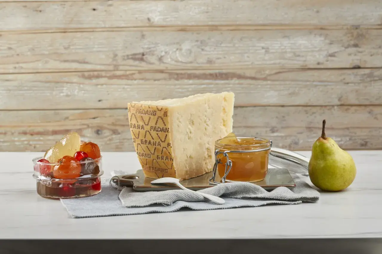Un pezzo di Grana Padano stagionato, un vasetto di miele dorato e frutta candita, pronti per un abbinamento delizioso.