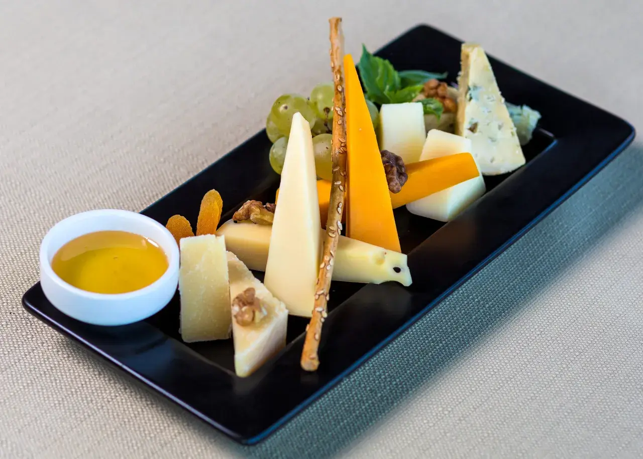 Piatto nero con vari formaggi, uva, noci, albicocche secche, grissini e una ciotolina di miele. Perfetti abbinamenti formaggi e frutta per un aperitivo.