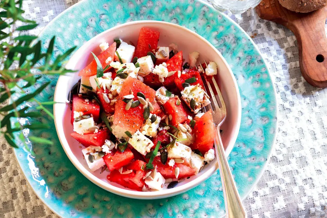 Insalata anguria e feta, fresca e colorata, con semi di girasole e zucca, guarnita con erbe aromatiche. Perfetta per l'estate.