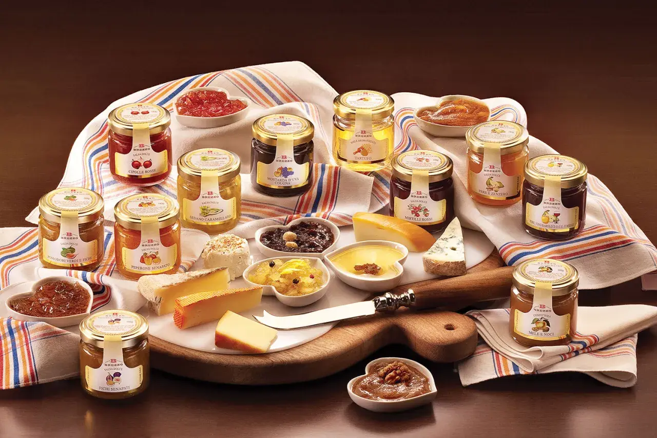 Una selezione di conserve, tra cui composta di fichi per formaggi, salse dolci e confetture, disposte su un tagliere con formaggi.