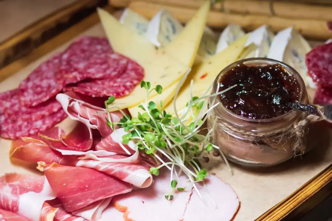 Un invitante antipasto salumi e formaggi con prosciutto, salame, formaggi misti, confettura e germogli freschi.