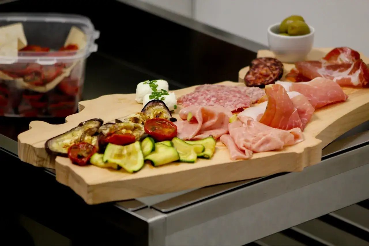 Tagliere con salumi, verdure grigliate e due forme di formaggio fresco.