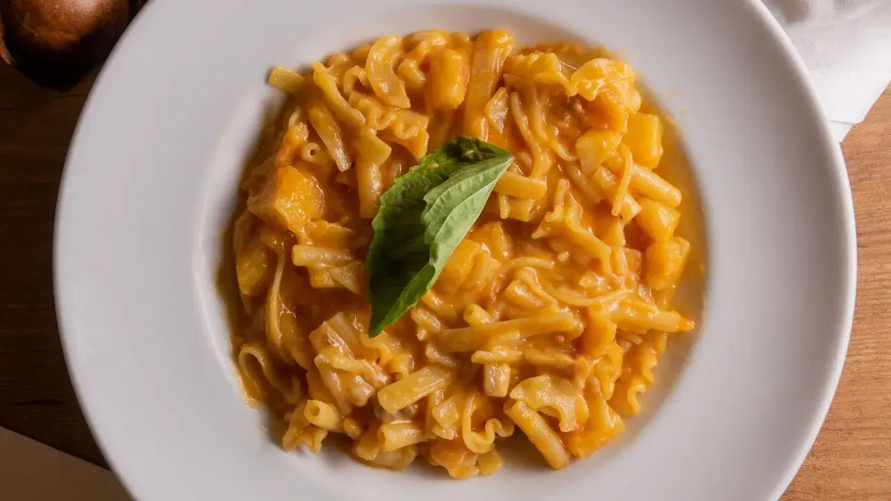 Un piatto di pasta patate e provola cremoso, guarnito con una foglia di basilico fresco.