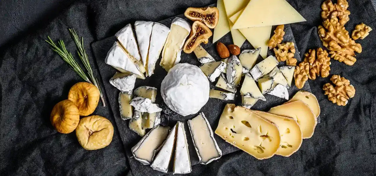 Un assortimento di formaggi salutari, fichi secchi, noci e rosmarino su una tavola scura.