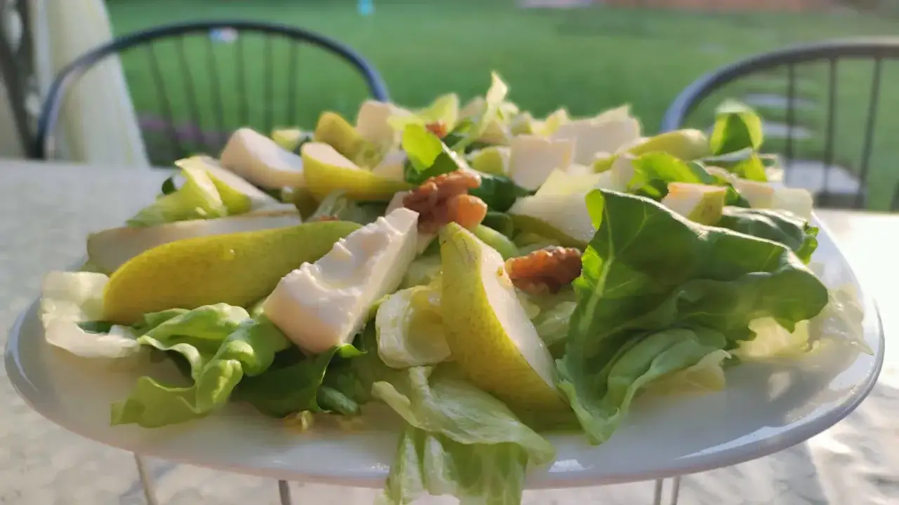 Deliziosa insalata con formaggio di capra, pere fresche e noci croccanti, servita su un piatto bianco con uno sfondo verde sfocato.