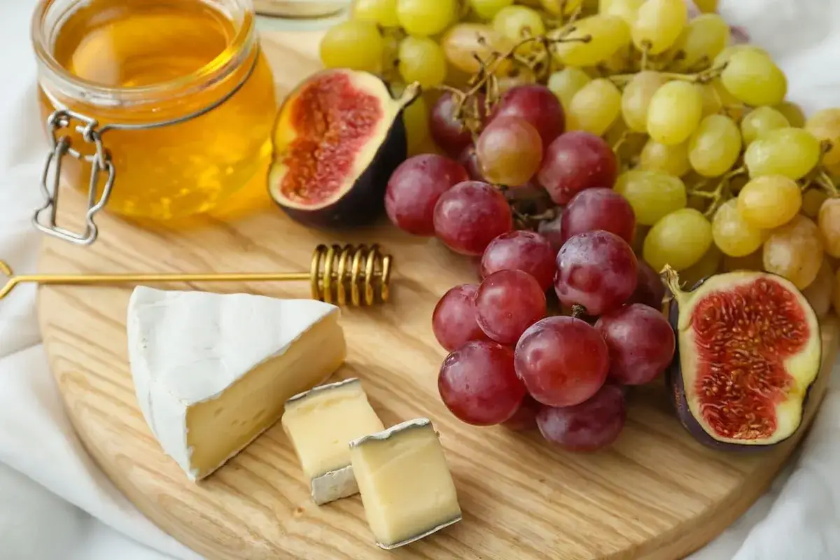 Tagliere con formaggio, uva, fichi e un vasetto di miele. Un abbinamento perfetto per un aperitivo con Grana Padano e miele.