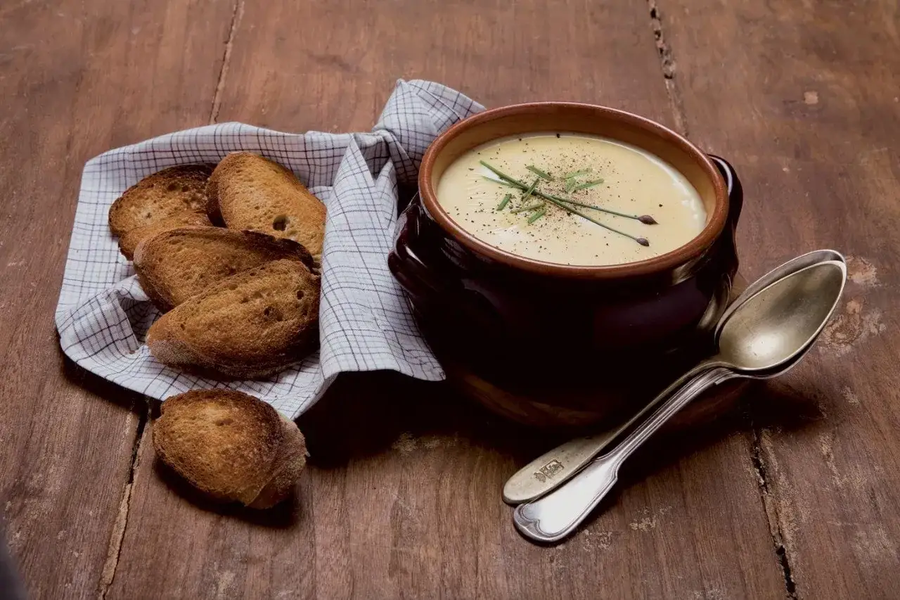 Ciotola di fonduta cremosa con crostini croccanti, erba cipollina e pepe. Ingredienti semplici per un piatto confortante.