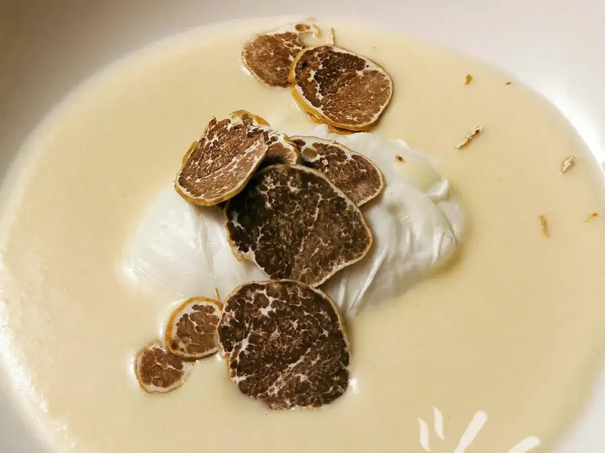 Uova al tartufo e formaggio: un uovo in camicia su crema di formaggio, guarnito con fette di tartufo nero.