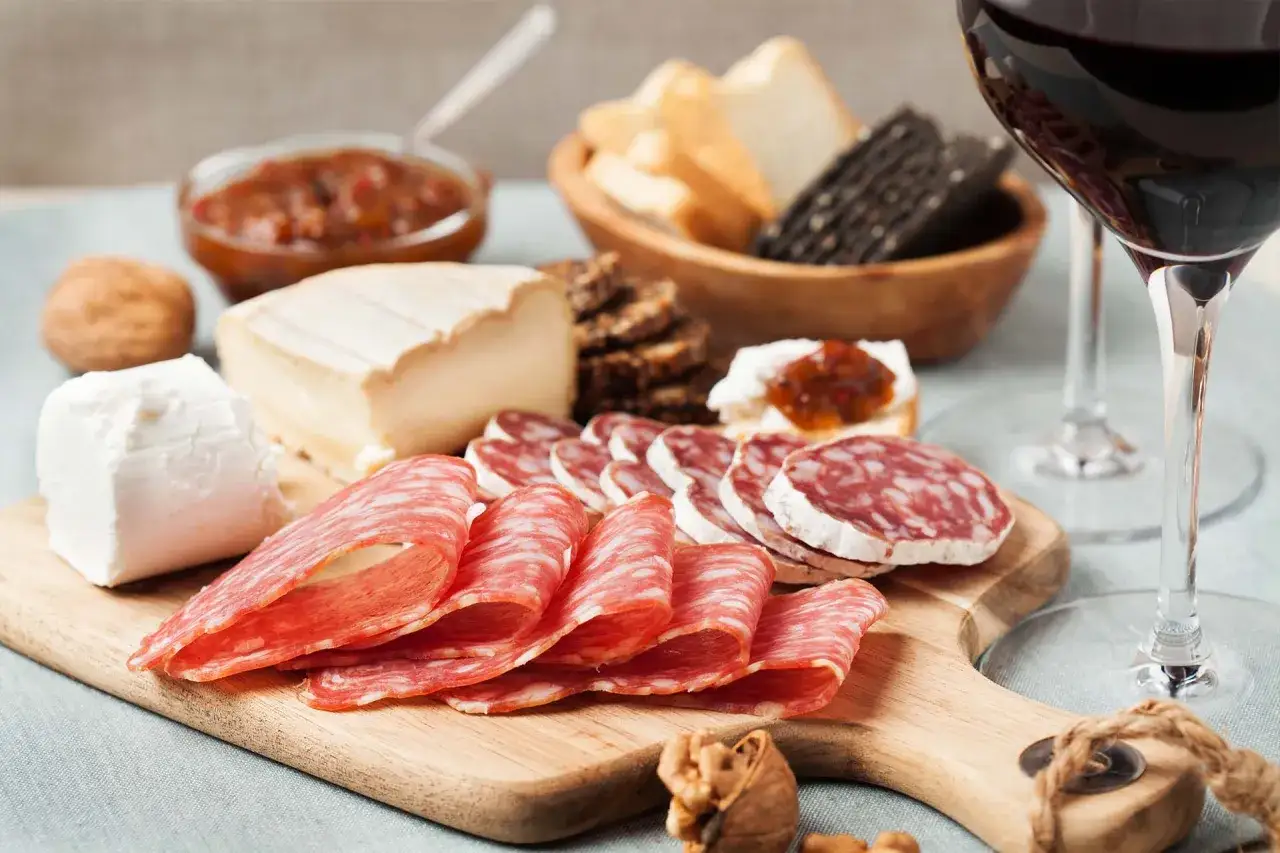 Perfetta presentazione tagliere aperitivo con salumi, formaggi, pane, noci e un bicchiere di vino rosso.