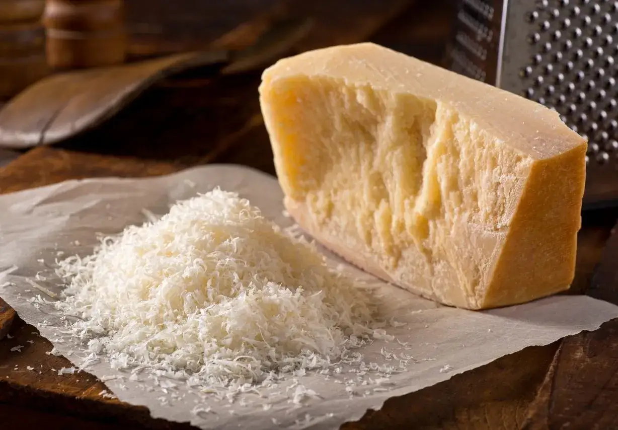 Un pezzo di Parmigiano Reggiano accanto a una montagna di formaggio grattugiato. Si può congelare il formaggio grattugiato per averlo sempre pronto.