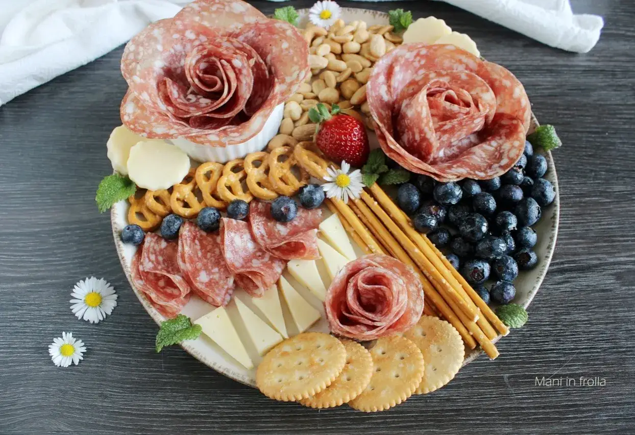 Tagliere di antipasti sfiziosi: salumi a rosa, formaggi, mirtilli, fragole, pretzel e grissini, un'esplosione di sapori e colori.