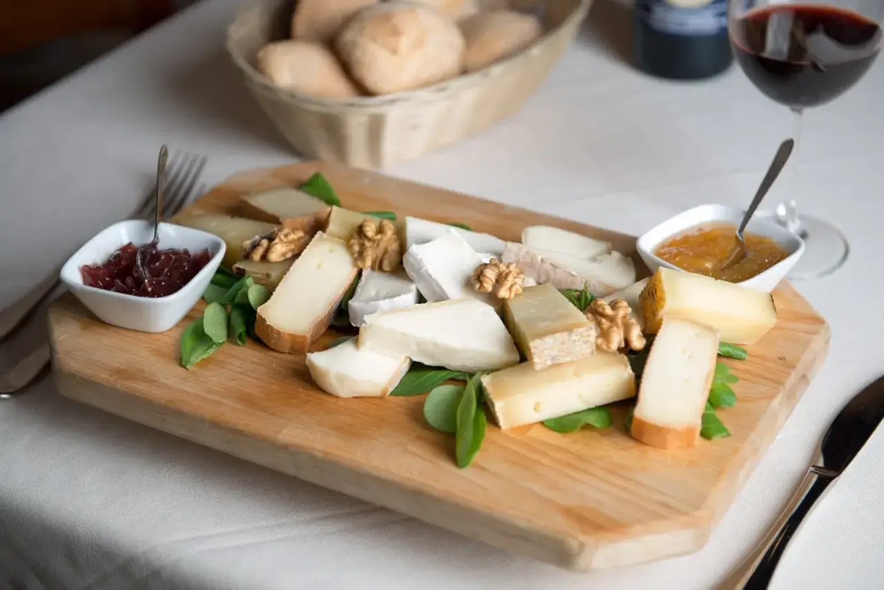 Assortimento di formaggi freschi e stagionati su tagliere di legno, accompagnati da marmellata e noci.