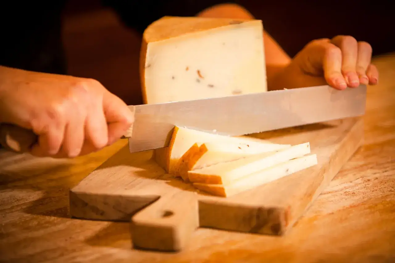 Mani che tagliano formaggio su un tagliere di legno. Fette sottili di formaggio sono già pronte.