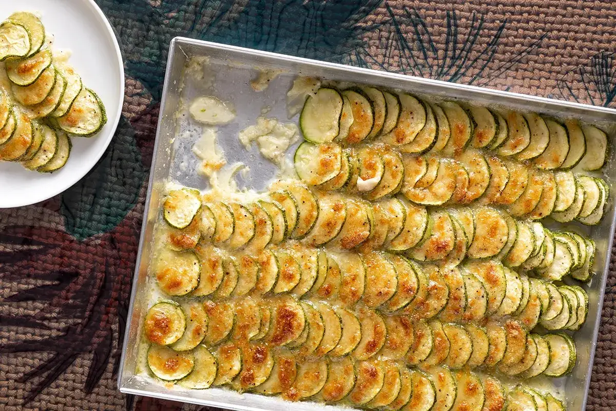 Zucchine al forno con mozzarella, disposte a raggiera in una teglia, dorate e filanti. Un piatto semplice e gustoso.
