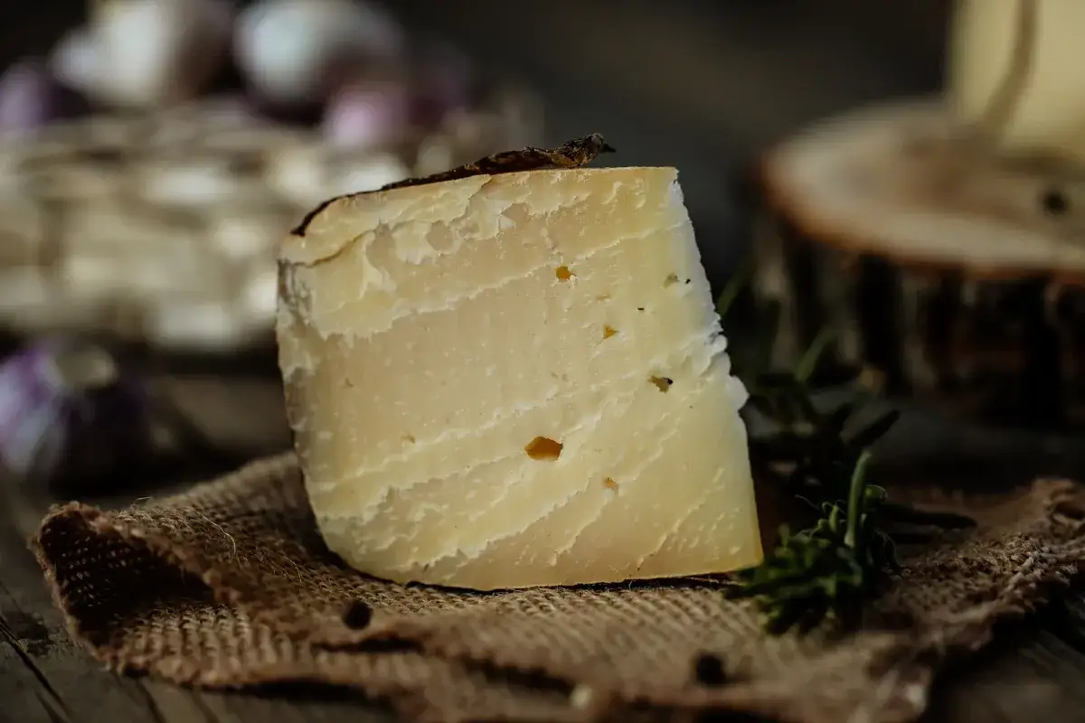 Un pezzo di fontina stagionata, ideale per chi cerca sapori autentici anche in gravidanza, su un tagliere rustico con aglio e rosmarino.