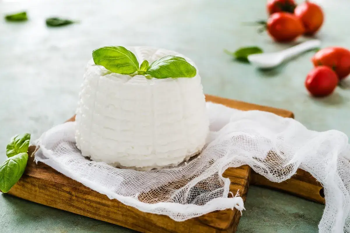 Formaggio fresco, un delizioso latticino e derivato, guarnito con basilico su un tagliere di legno, con pomodorini sullo sfondo.