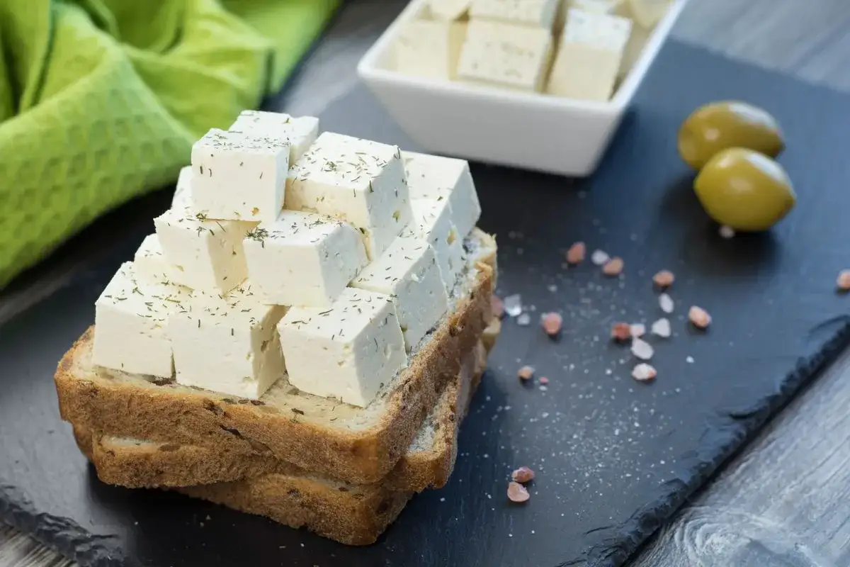 Fetta di pane con cubetti di formaggio bianco cosparsi di erbe aromatiche. Un'idea su come sostituire la feta in modo gustoso.