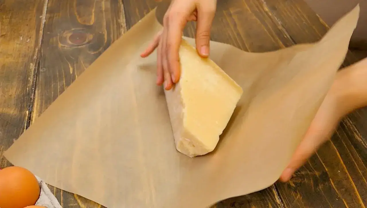 Mani che avvolgono un pezzo di parmigiano in carta oleata. Scopri come conservare il parmigiano in frigo per mantenerlo fresco.