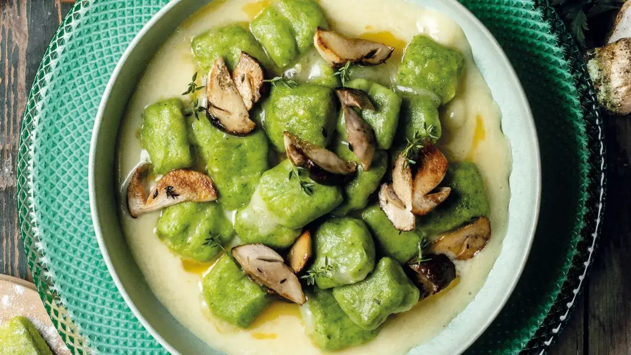Gnocchi verdi in cremosa fonduta, guarniti con funghi trifolati e timo. Un piatto invitante che celebra i sapori autunnali.