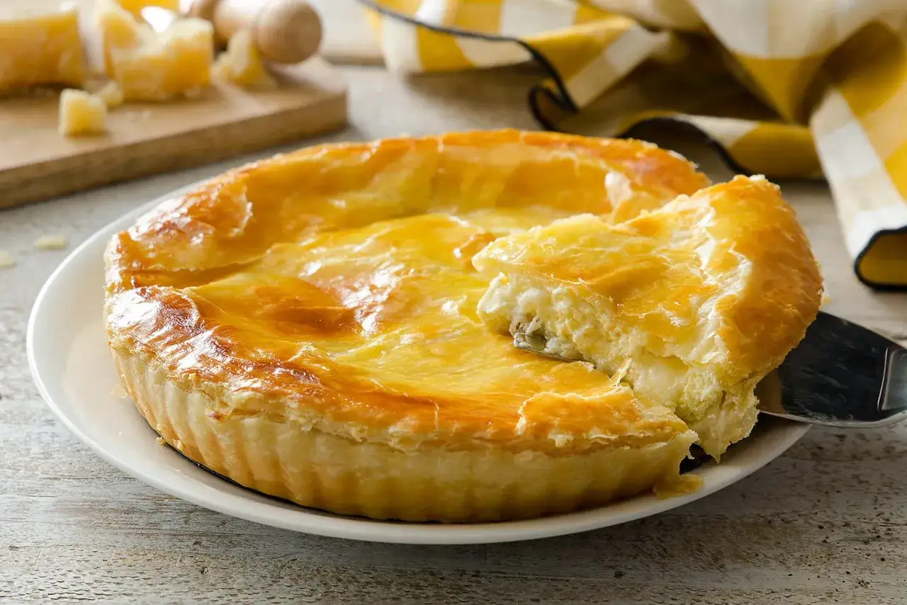 Torta salata dorata, perfetta per le tue ricette con formaggio. Un pezzo viene sollevato con una paletta, rivelando il ripieno cremoso.