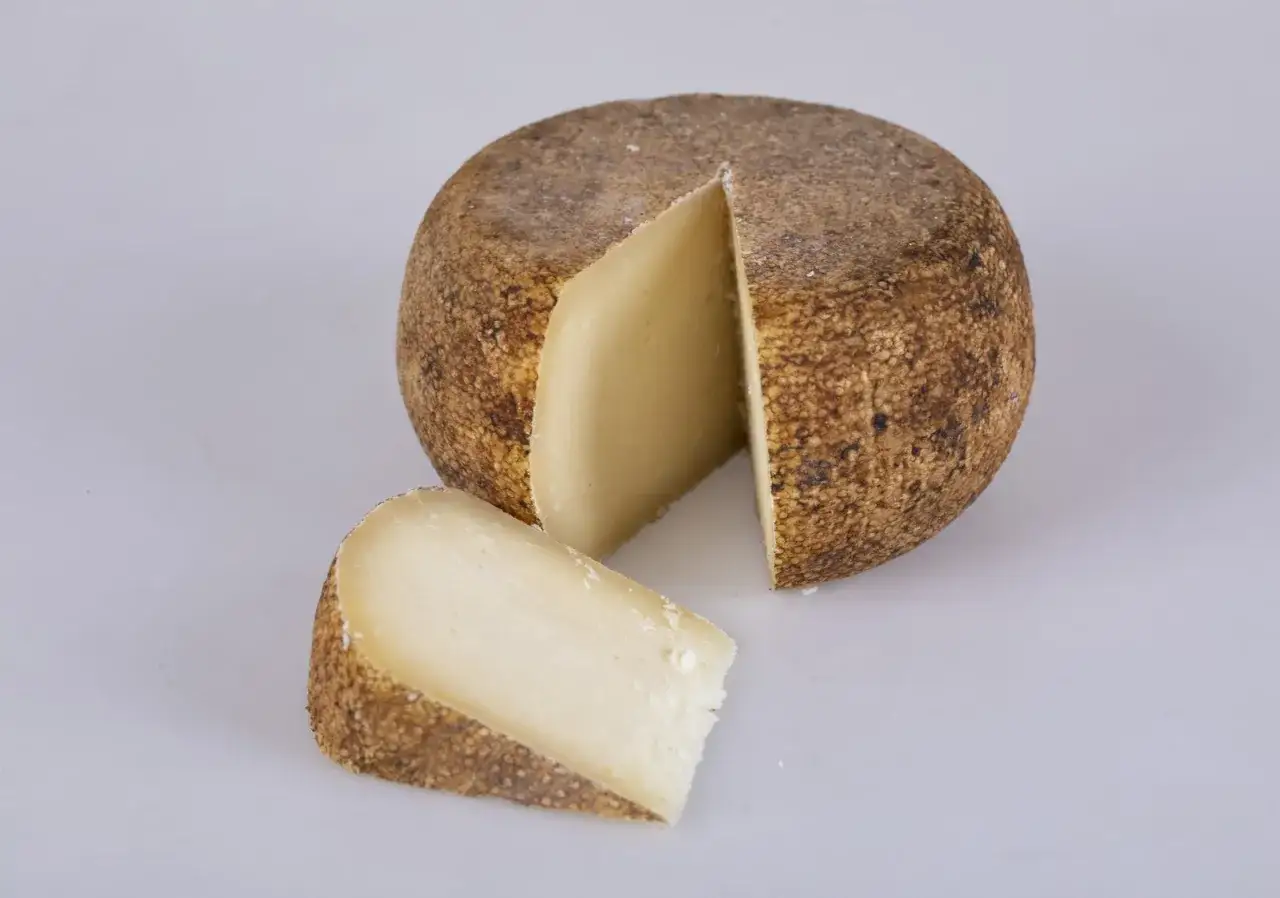 Un pezzo di cacio stagionato, con crosta ruvida e pasta chiara, pronto per essere gustato.