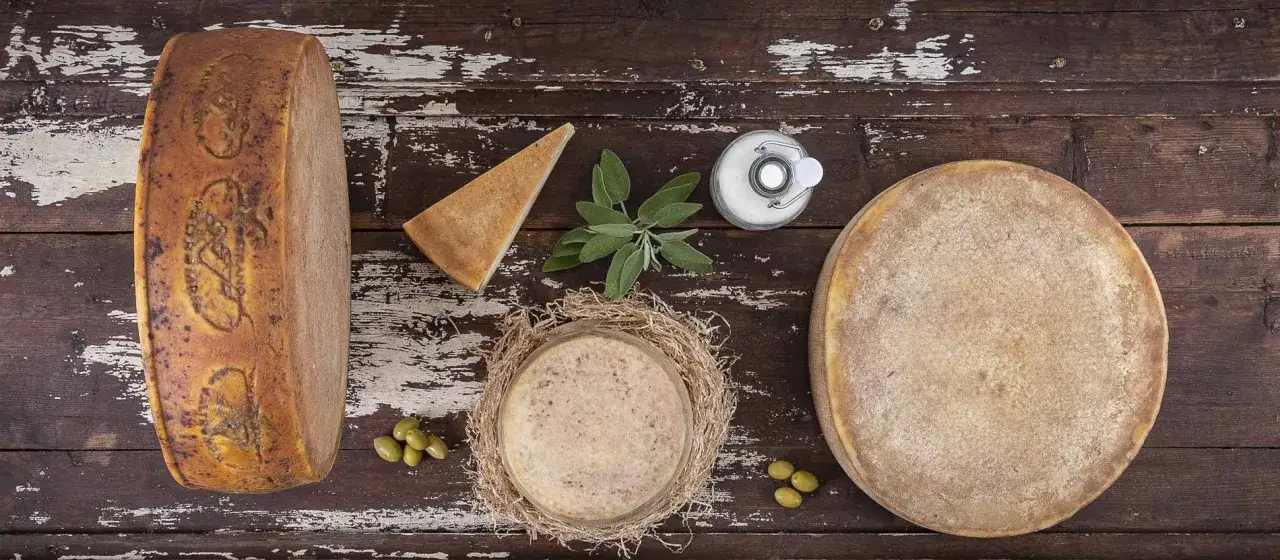 Formaggi stagionati, tra cui quelli con più colesterolo, disposti su un tavolo di legno. Si notano olive, salvia e un barattolo di sale.