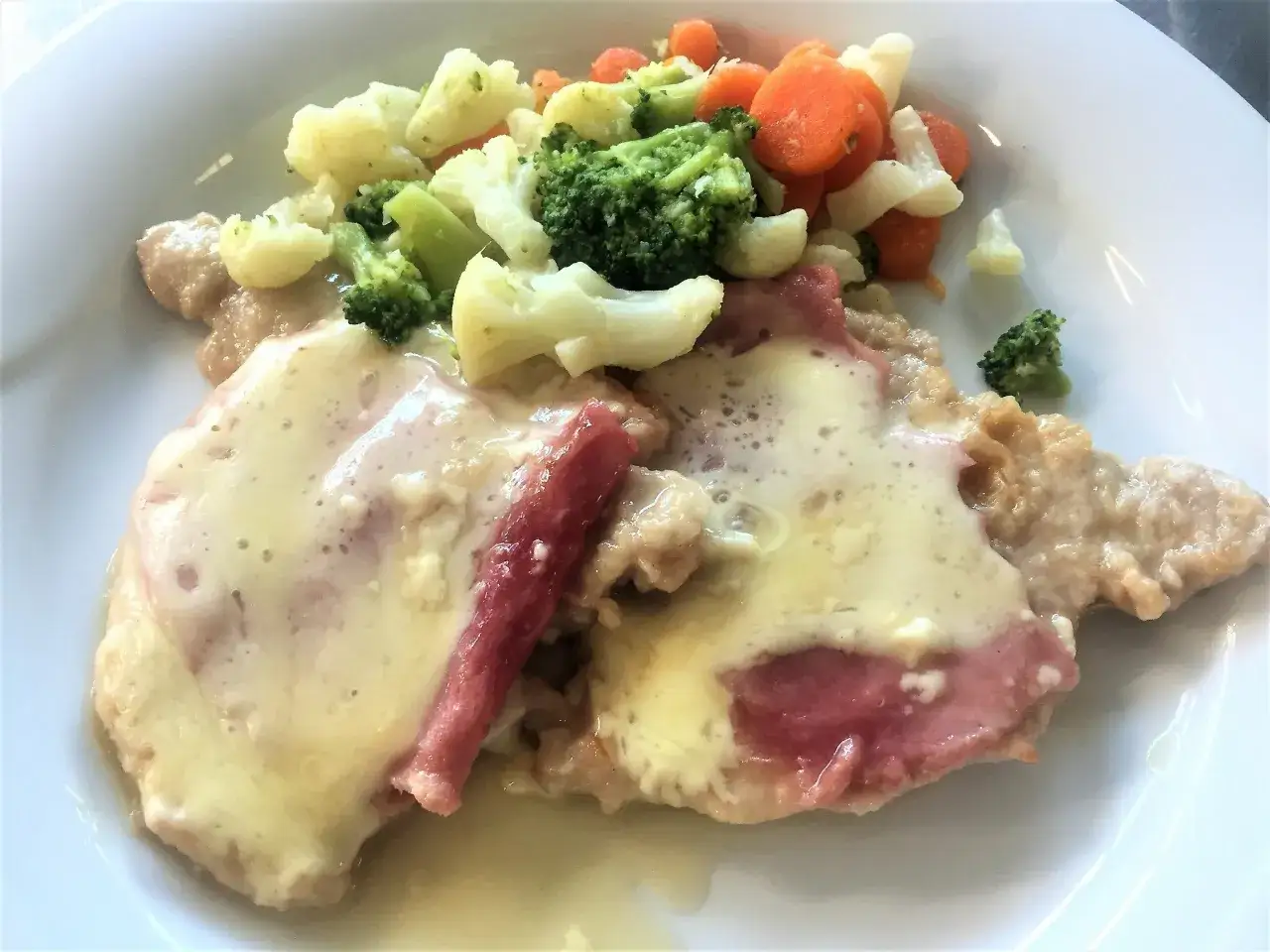 Scaloppine alla Valdostana con prosciutto e formaggio fuso, accompagnate da un contorno di verdure miste al vapore.