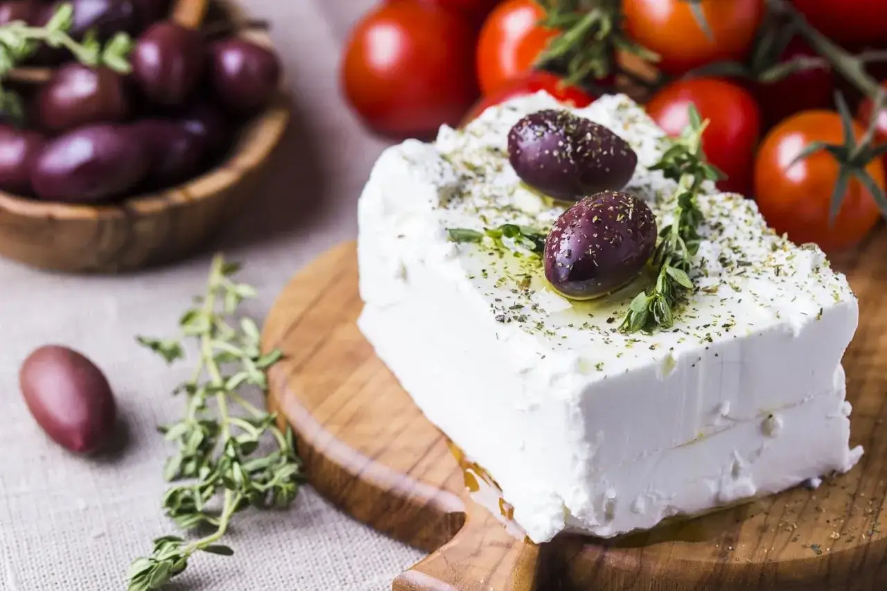 Un blocco di feta condito con olive e erbe aromatiche, pronto per essere gustato. Attenzione, la feta contiene lattosio.