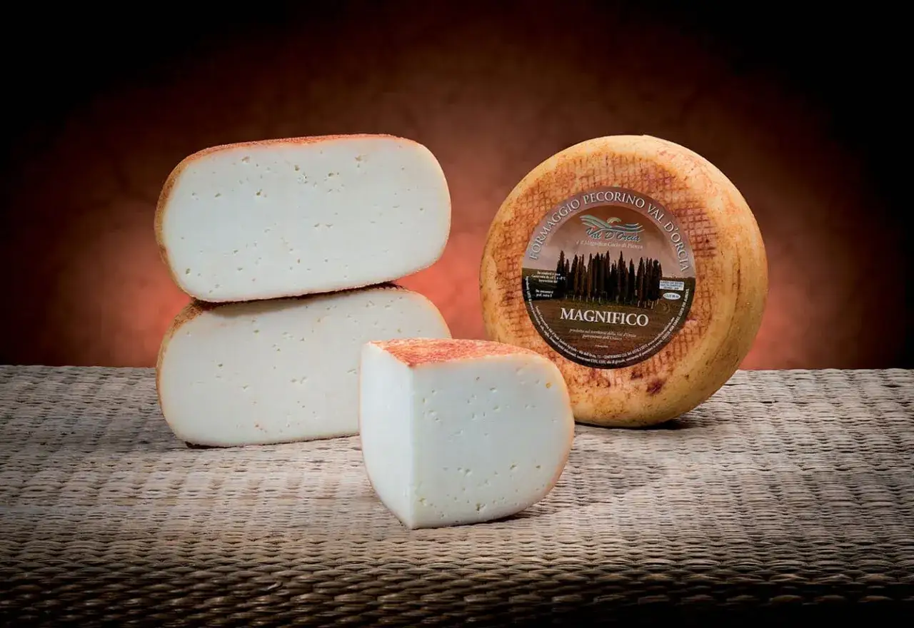 Formaggio pecorino semistagionato, con una forma intera e pezzi tagliati, su un piano intrecciato.