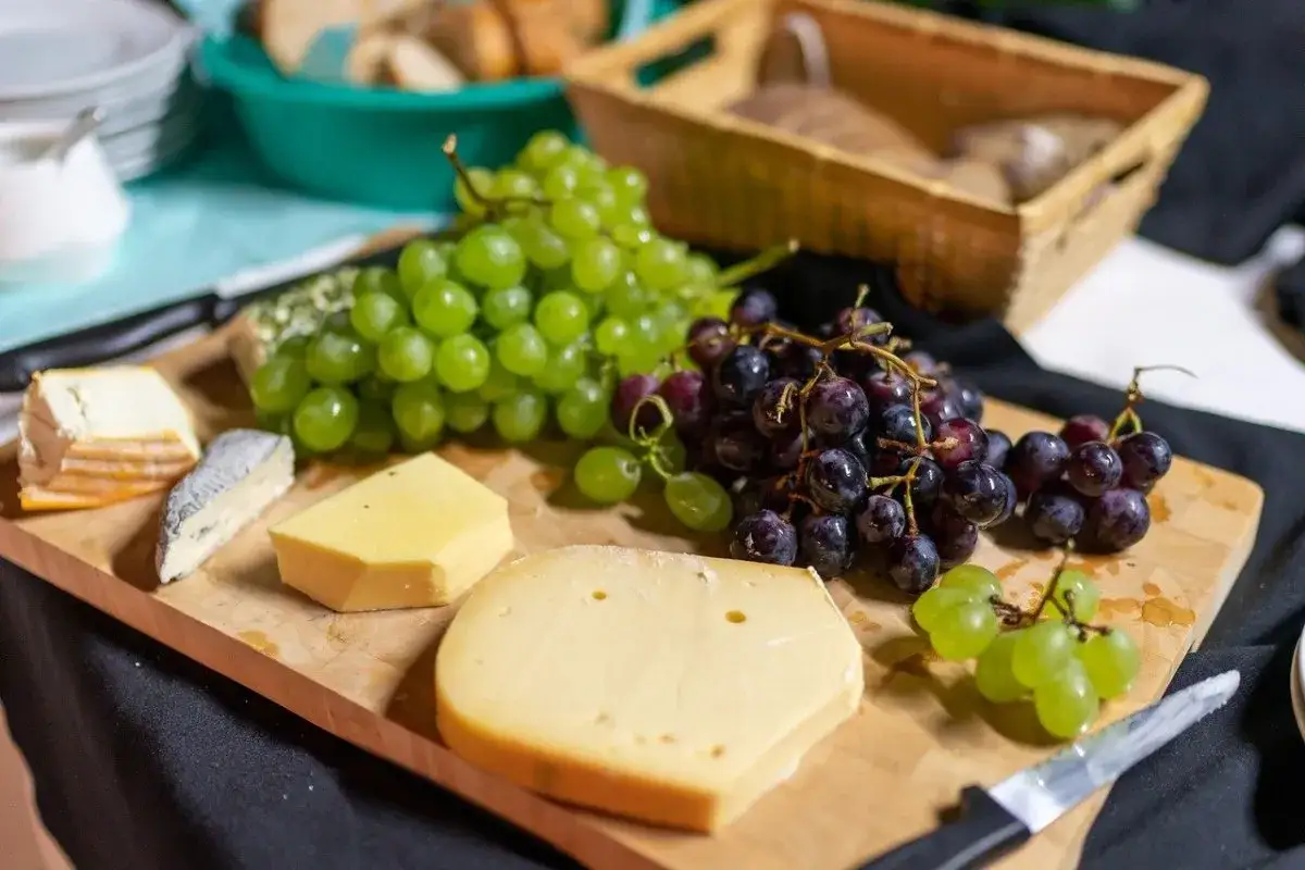 Assortimento di formaggi siciliani e grappoli d'uva su tagliere di legno.