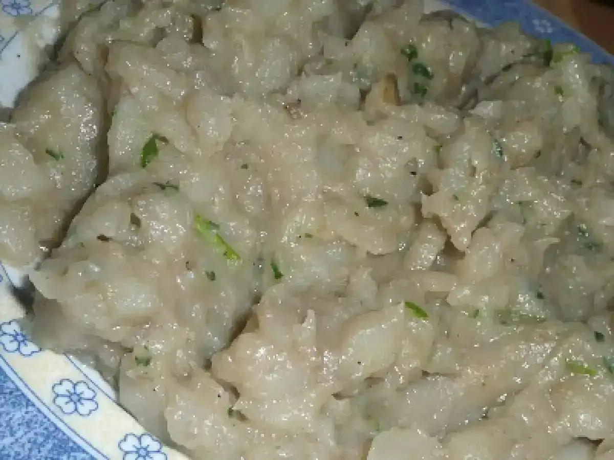 Una cremosa fonduta di Asiago, arricchita da erbe aromatiche, servita in un piatto con decorazioni floreali blu.
