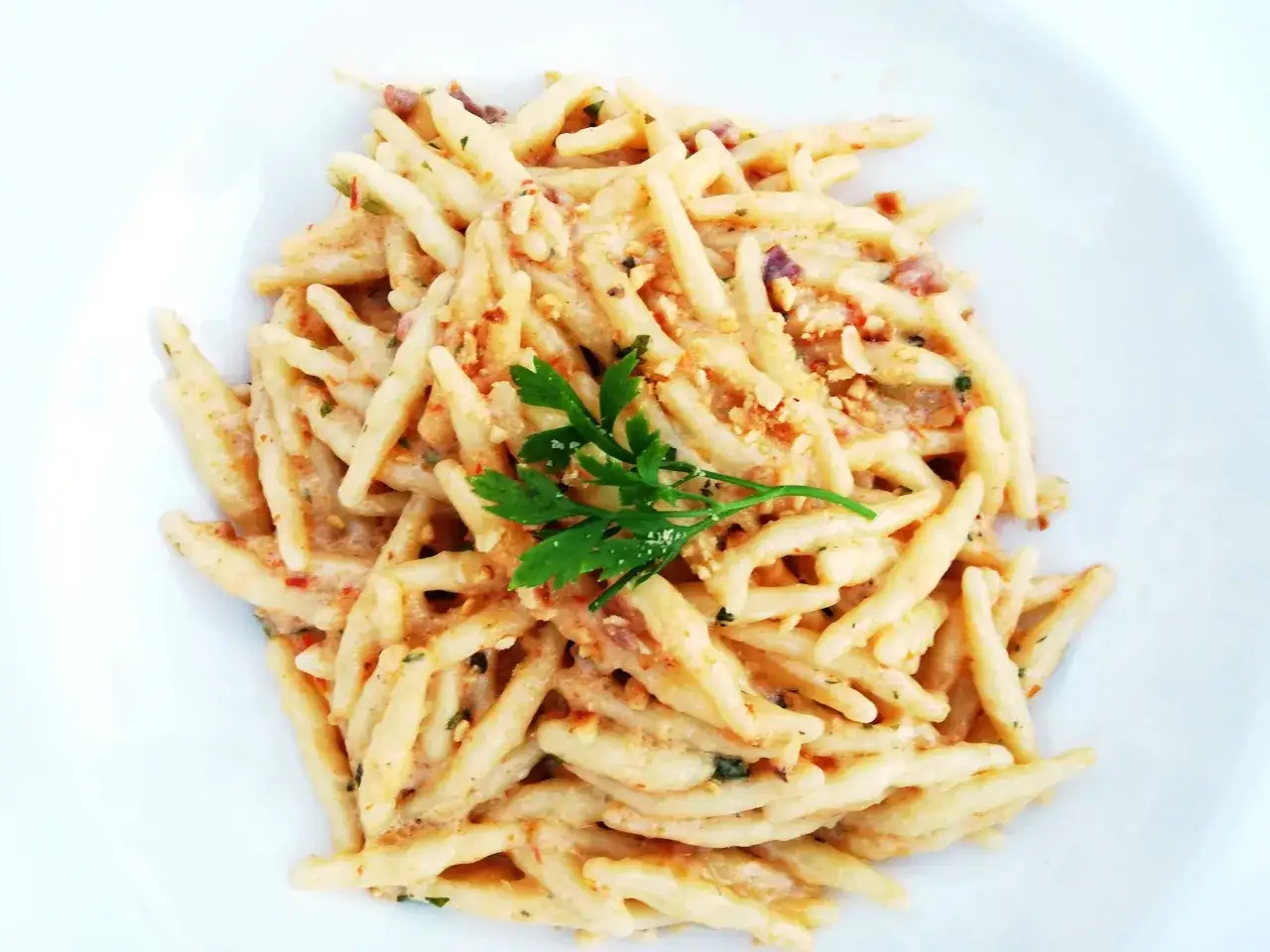 Un piatto di trofie cacio e pepe, condite con una cremosa salsa al formaggio e pepe nero, guarnite con prezzemolo fresco.