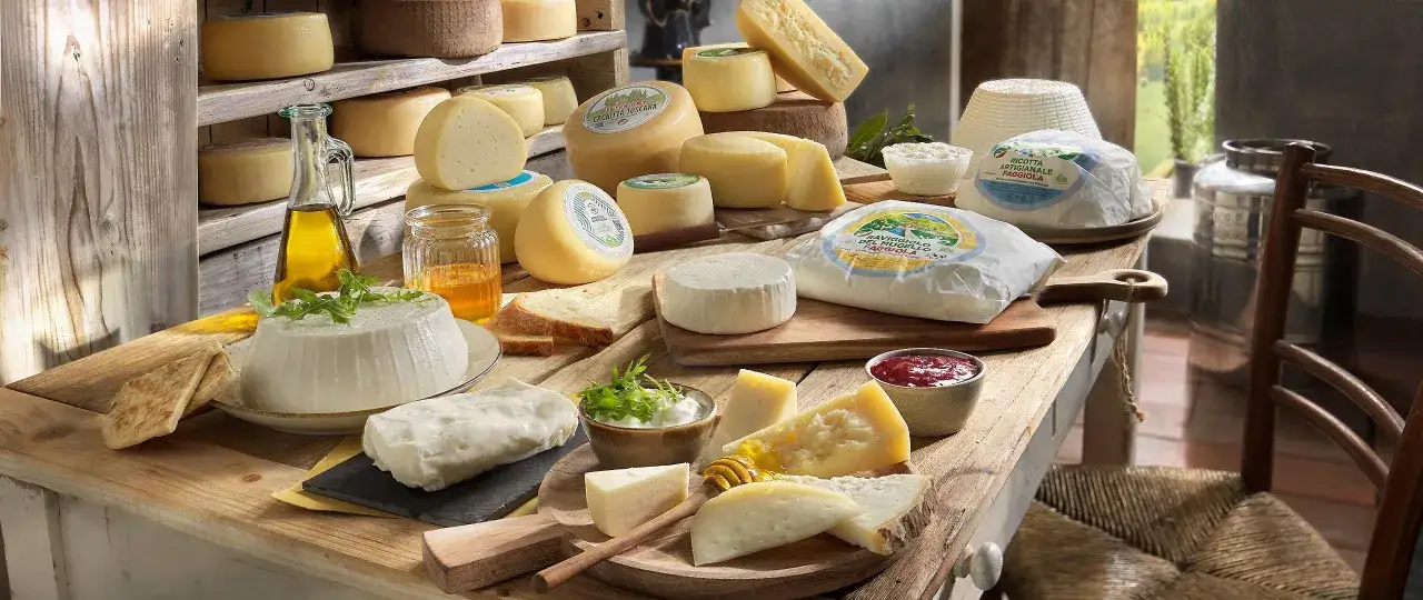 Varietà di formaggi, tra cui un formaggio semistagionato, ricotta e caciotta, disposti su un tavolo di legno con miele, pane e olio.